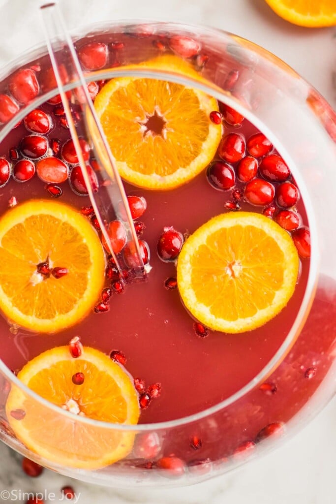 overhead view of a sphere punch bowl full of christmas punch with orange slices and cranberries floating in it