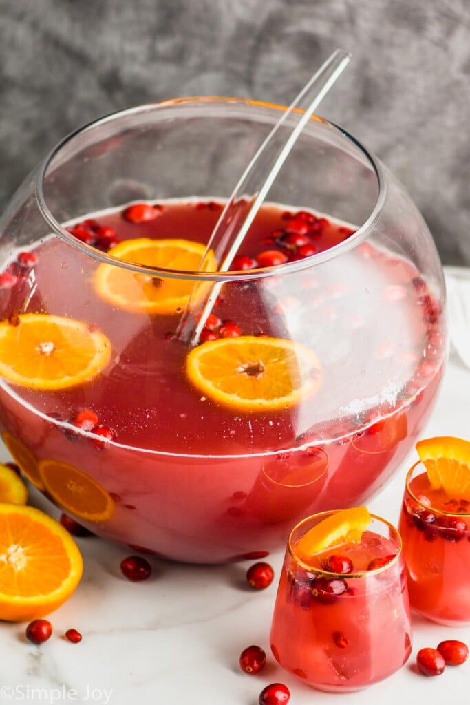 a sphere punch bowl full of red holiday punch recipe with cranberries and orange slices floating in it