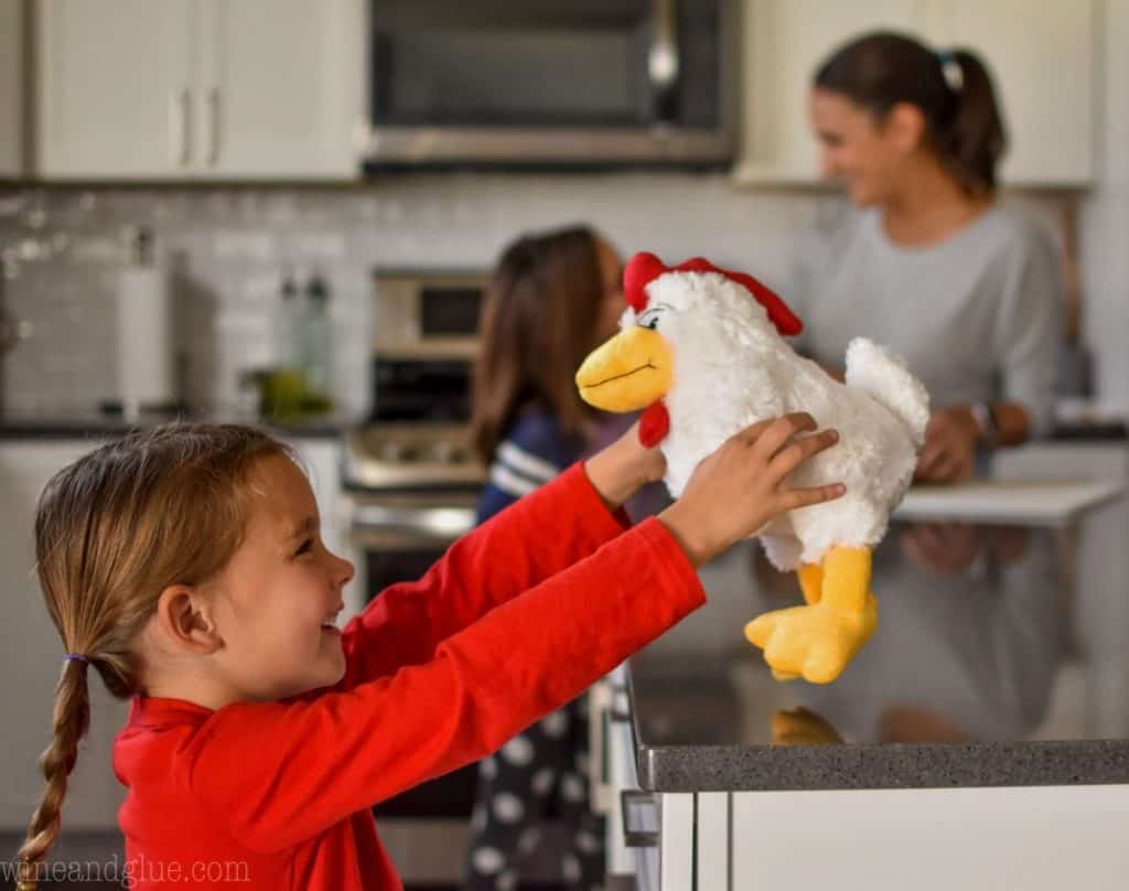 picture of a little girl in a kitchen playing with a stuffed chicken