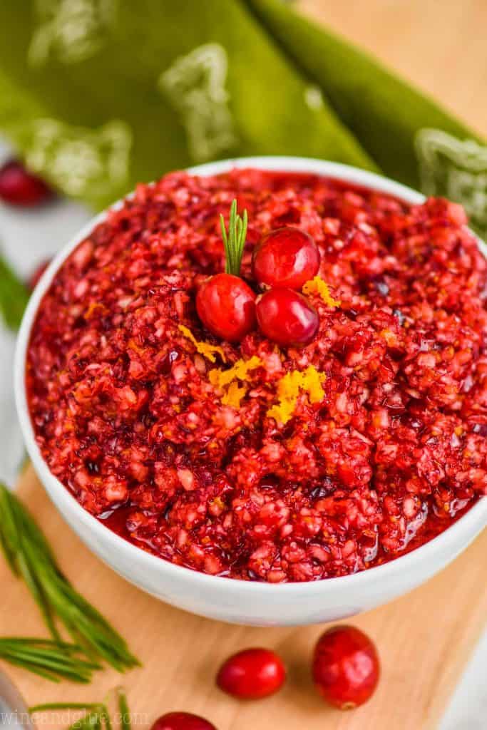 close up picture of cranberry orange relish recipe in a white bowl on a cutting board with fresh cranberries and rosemary around it