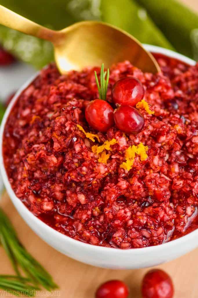 up close picture of a white bowl full of cranberry relish being spooned up by a golden spoon