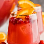 a gold rimmed wine glass full of non alcoholic holiday punch with cranberries floating in it and an orange wedge