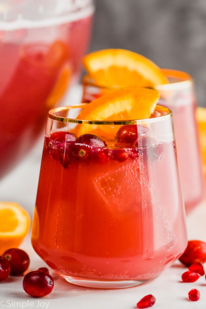 a gold rimmed wine glass full of non alcoholic holiday punch with cranberries floating in it and an orange wedge