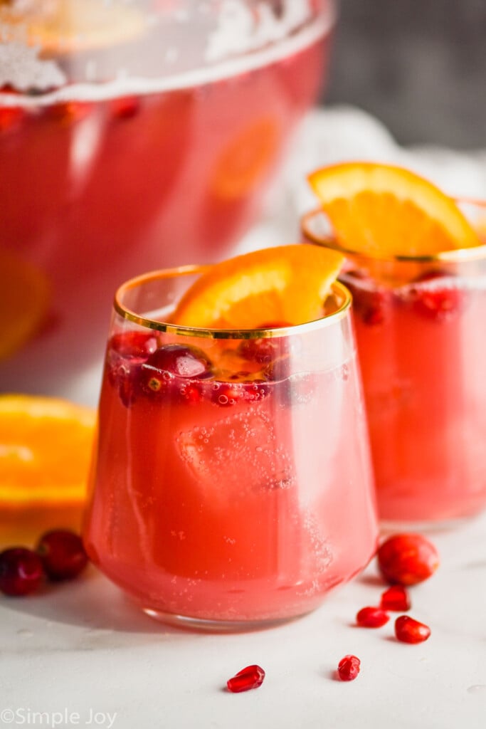 two glasses full of red holiday punch recipe with cranberries floating and orange slices in it