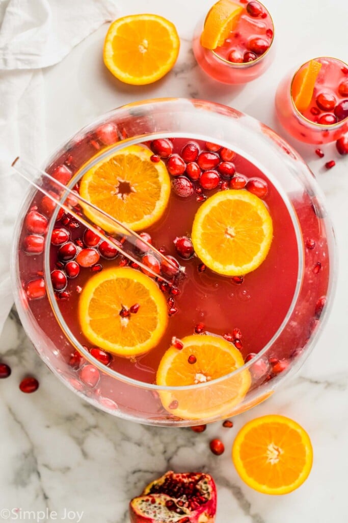 overhead view of sphere punch bowl with non alcoholic Christmas punch with orange slices and cranberries floating in it and two glasses full of it