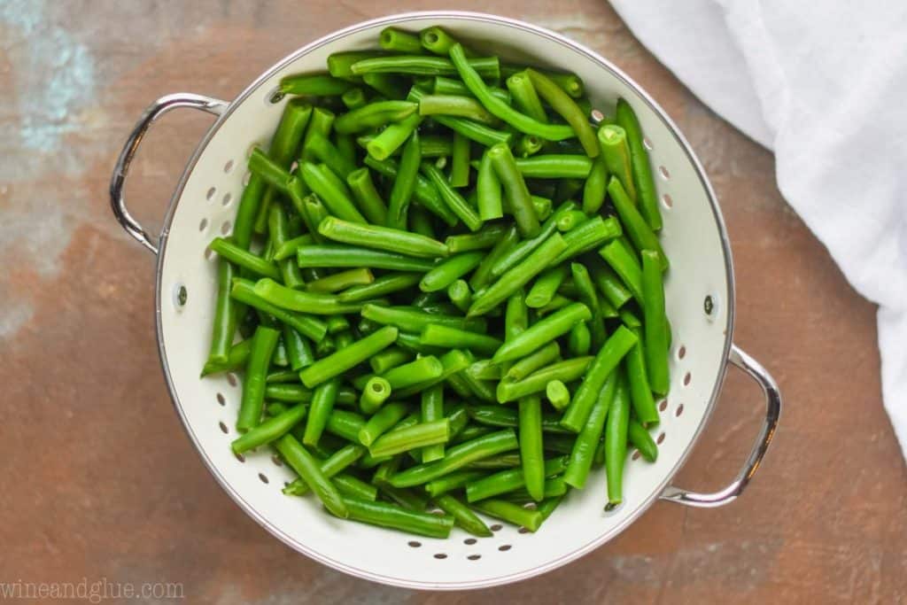 overhead photo of green beans that have been par boiled in a white metal colander