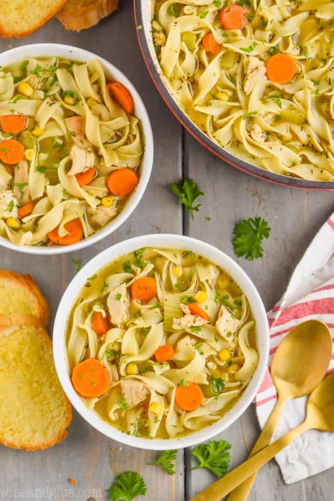 overhead view of two bowls of turkey noodle soup with the stock pot full of the rest of the soup next to it, some buttered toast for dipping next to it