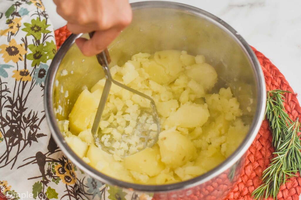 a hand mashing cooked potatoes that are in an instant pot