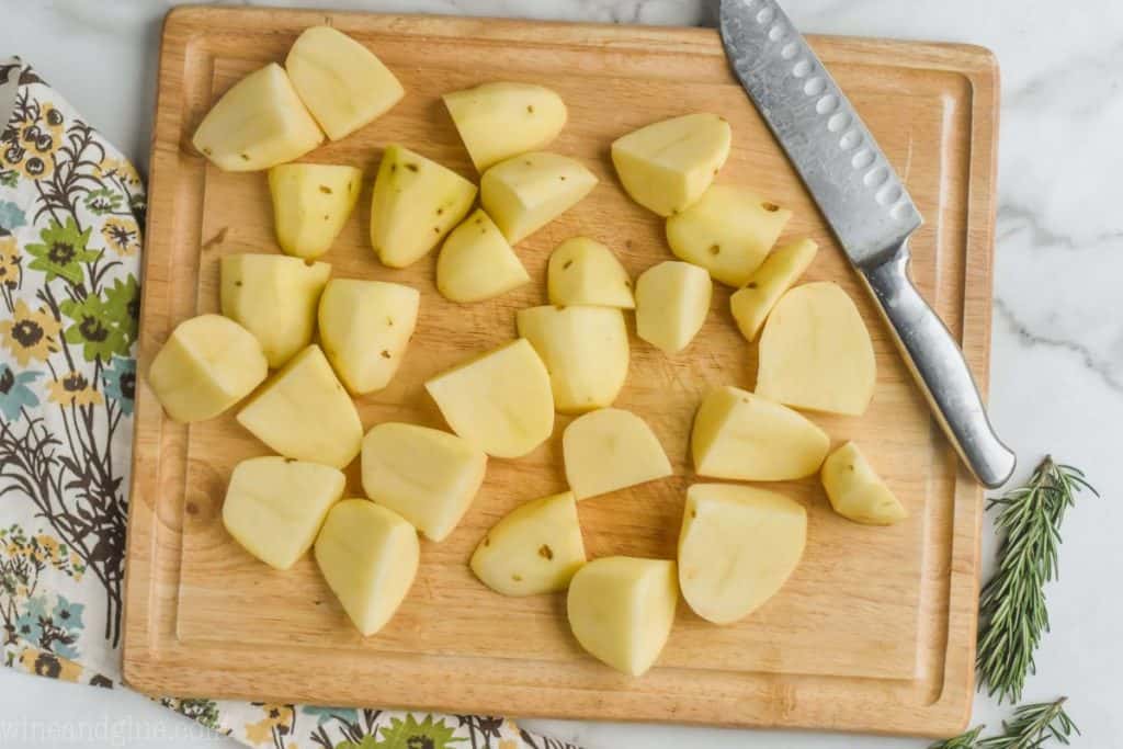 overhead of a wooden cutting board with potatoes that have been peeled and quartered