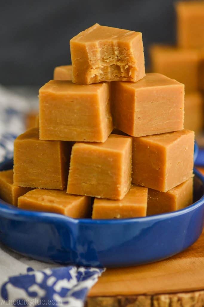 a pyramid of peanut butter fudge piled into a small blue dish with handles on a white napkin and a wood block. The top block has a small bite out of it