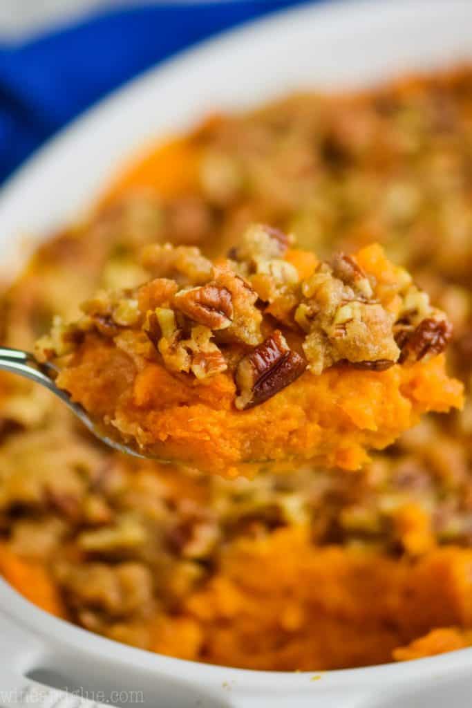 a close up of a spoonful of sweet potato casserole topped with pecans