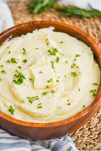 instant pot mashed potatoes in a wooden bowl with parsley garnish and a square of butter on top