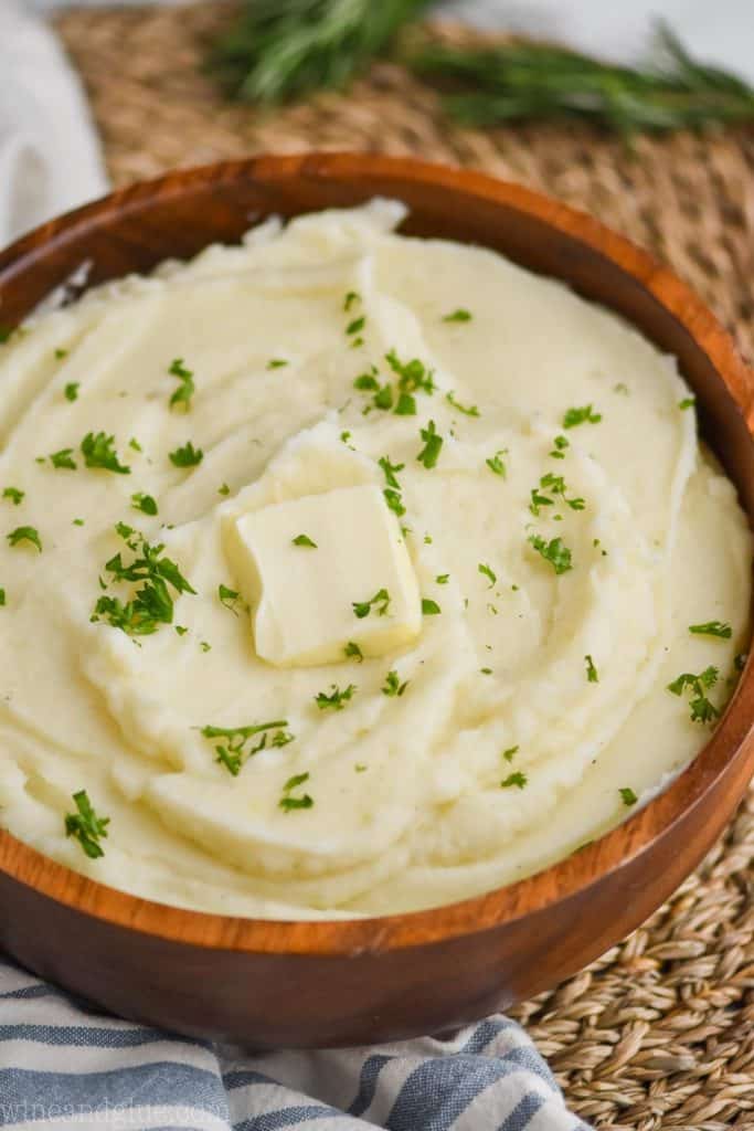 instant pot mashed potatoes in a wooden bowl with parsley garnish and a square of butter on top