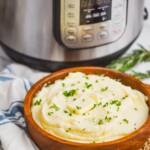 mashed potatoes made in the instant pot in a wooden bowl sitting in front of an instant pot, with a cloth napkin next to it