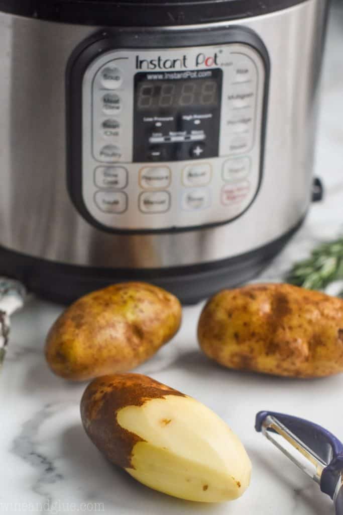 three russet potatoes for creamy mashed potatoes, one half peeled, sitting in front of an instant pot