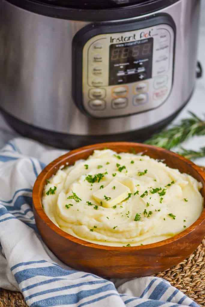 mashed potatoes made in the instant pot in a wooden bowl sitting in front of an instant pot, with a cloth napkin next to it