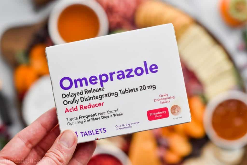A close up photo of a box of Omeprazole ( an acid reducer), and in the background, the cheese board with various crackers and cheeses.