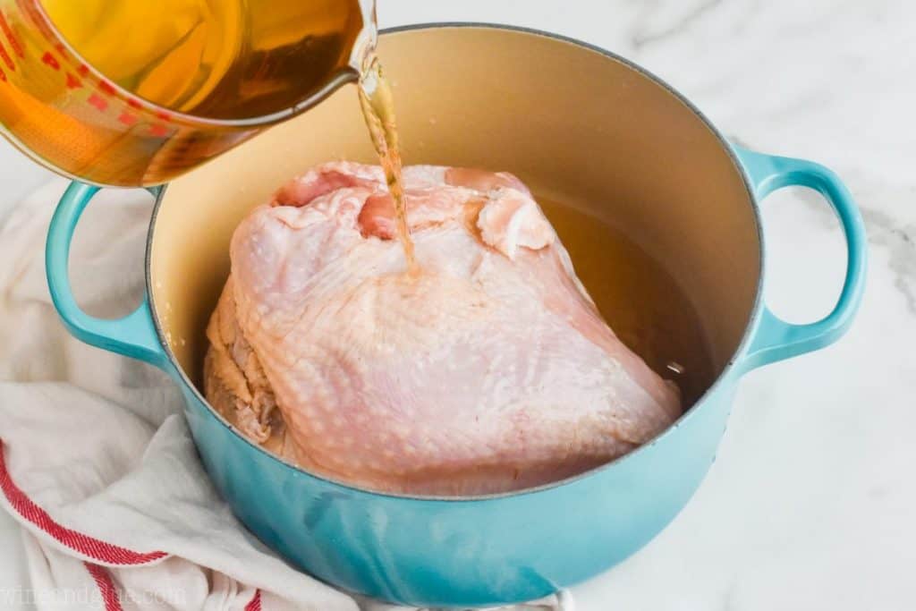 a raw turkey in a stock pot with turkey brine being poured over it