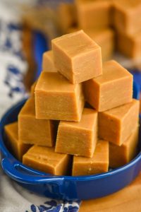 a pyramid of peanut butter fudge piled into a small blue dish with handles on a white napkin and a wood block