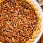 overhead view of a full pecan pie recipe in a white ceramic pie plate with an antique pie server next to it and sitting on a wire rack