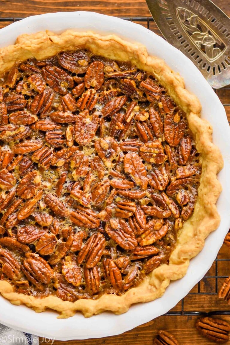 overhead view of a full pecan pie recipe in a white ceramic pie plate with an antique pie server next to it and sitting on a wire rack