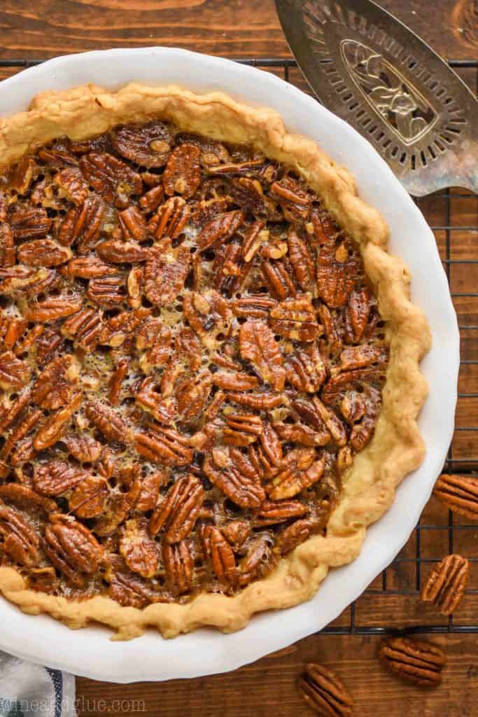 overhead view of a full pecan pie recipe in a white ceramic pie plate with an antique pie server next to it and sitting on a wire rack