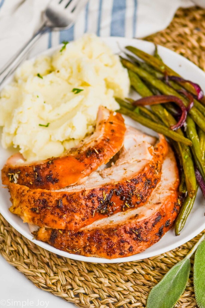 cut up baked turkey breast on a plate with mashed potatoes and green beans