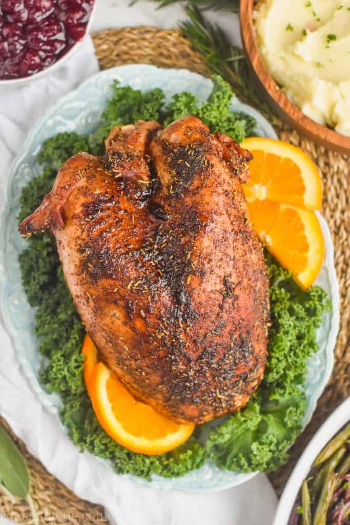 overhead view of a roast turkey breast sitting on a bed of greens with orange slices around it