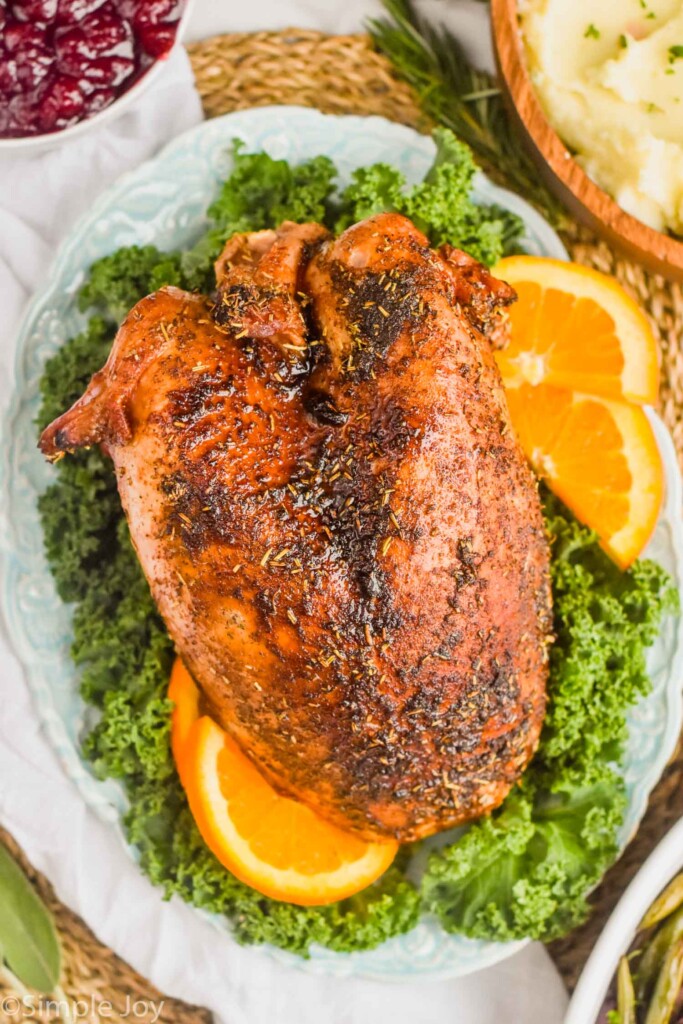 overhead view of a roast turkey breast sitting on a bed of greens with orange slices around it