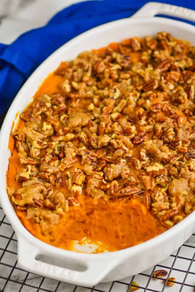 side view of a sweet potato casserole that is topped with pecans that has some of the dish scooped out, sitting on a wire cooling rack