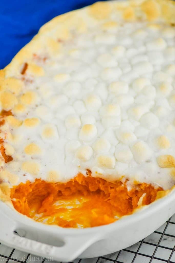white casserole dish from the side with sweet potato casserole topped with marshmallow that has been scooped out