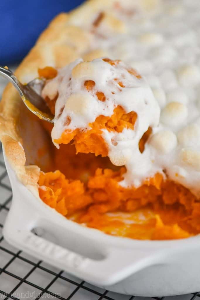 close up of a spoon dishing up sweet potato casserole recipe that is topped with marshmallows