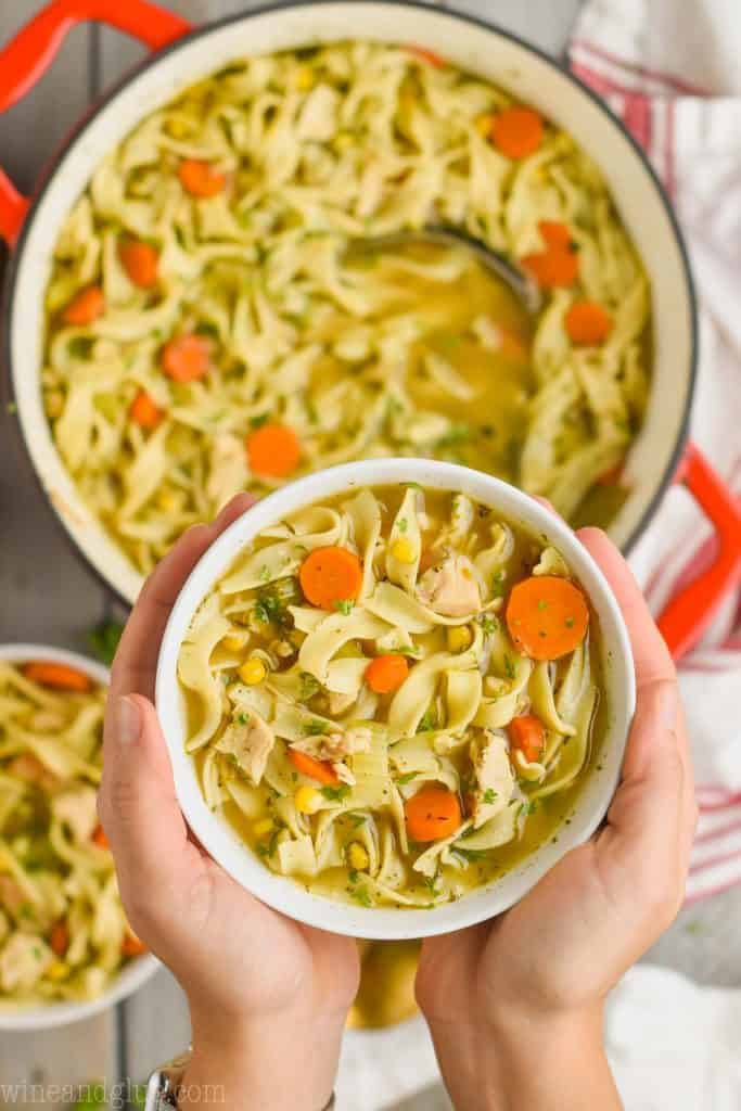 two hands holding a bowl of turkey noodle soup made from thanksgiving leftovers over the larger pot of soup