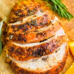 turkey breast that has been cooked and is cut up sitting on a cutting board with orange slices and rosemary sprigs