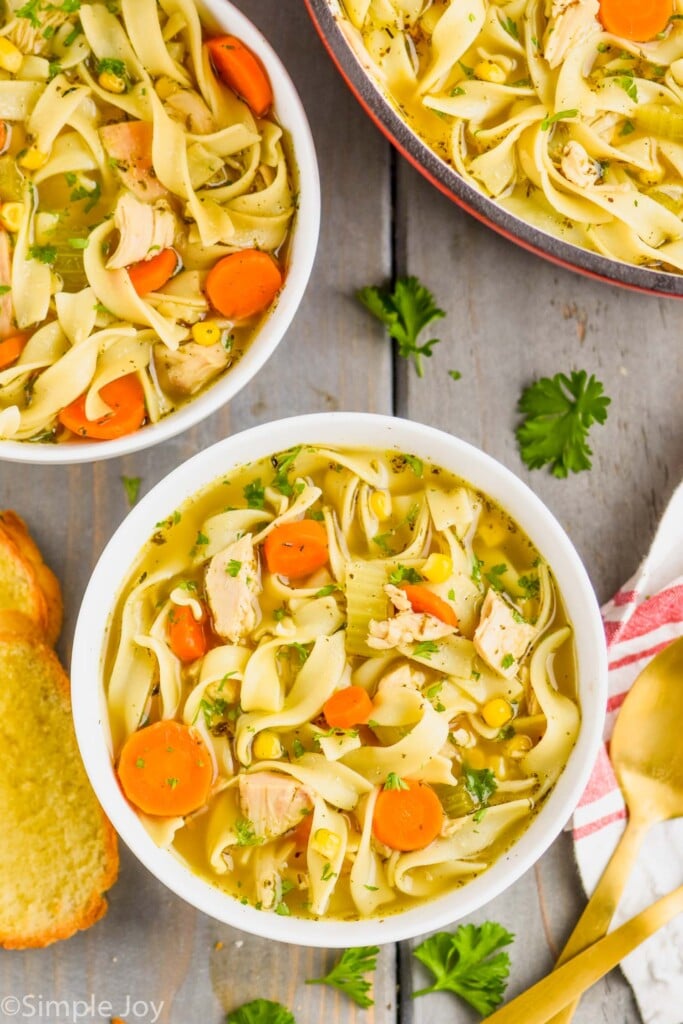 overhead view of two bowls of turkey noodle soup with the stock pot full of the rest of the soup next to it, some buttered toast for dipping next to it