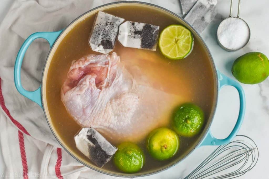 overhead view of a teal stock pot full of raw turkey breast in a brine with lime wedges and tea bags