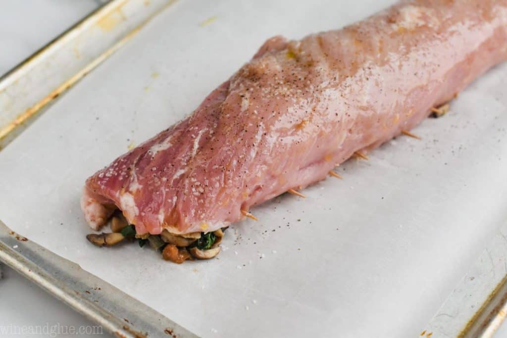a stuffed pork loin that is on a parchment paper lined baking sheet and ready for the oven