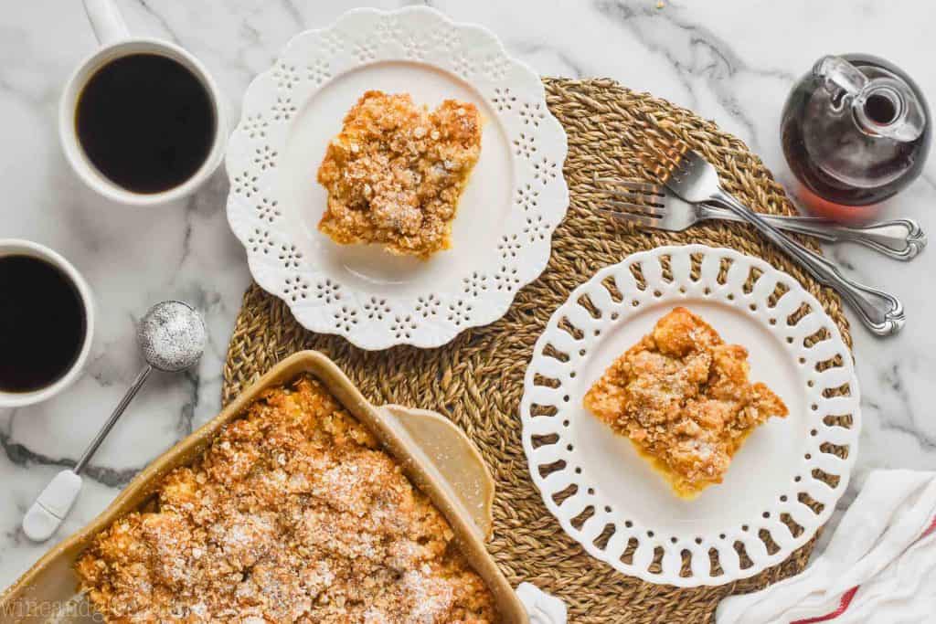 overhead view of breakfast scene with two white plates holding breast French toast casserole, two forks, two cups of coffee, and the rest of the casserole in a ceramic baking dish