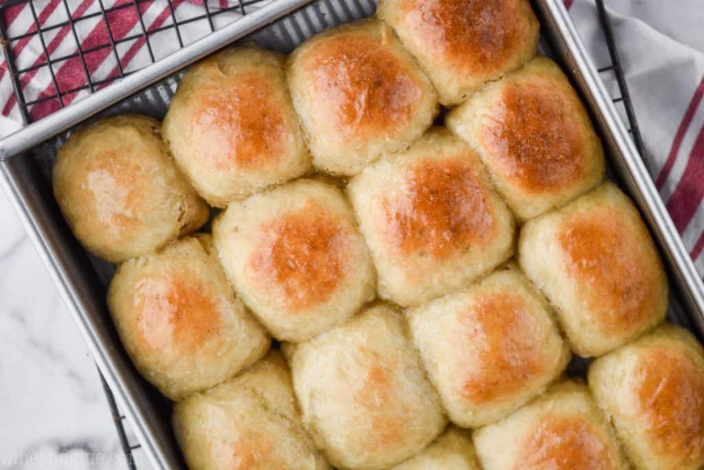 an overhead picture of baked dinner rolls in a metal baking dish resting on a wire rack