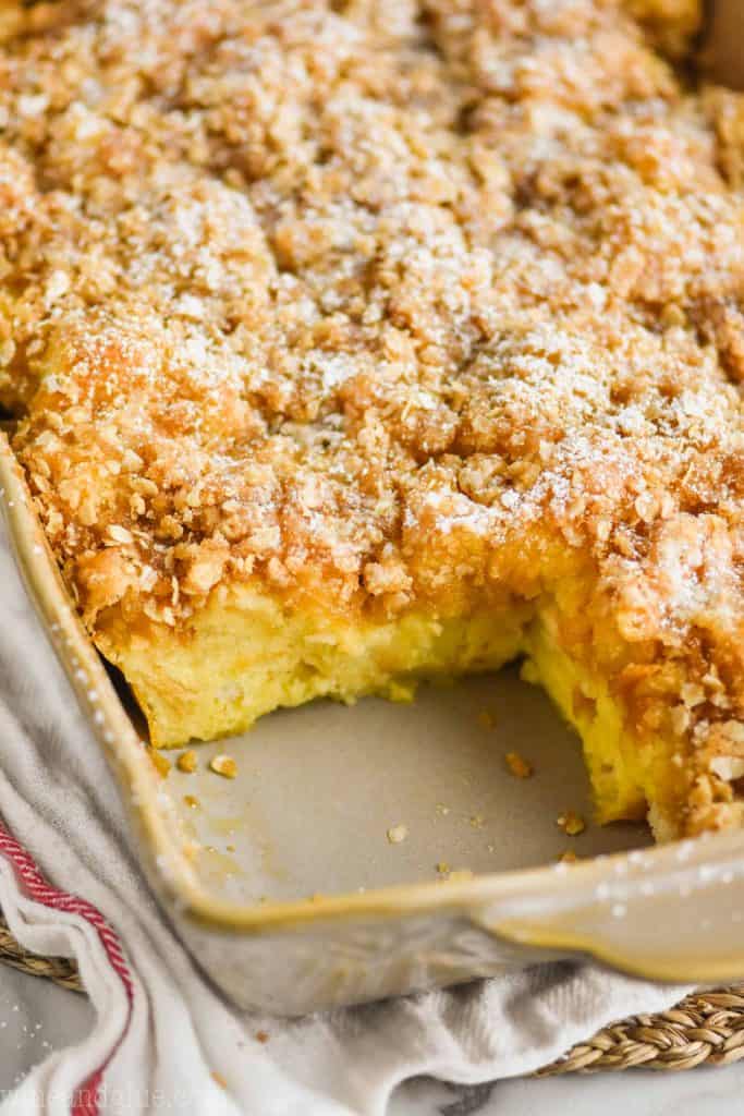 close up of a French toast casserole recipe that is still in the baking dish with one piece missing, it is topped with a crispy streusel topping and powdered sugar