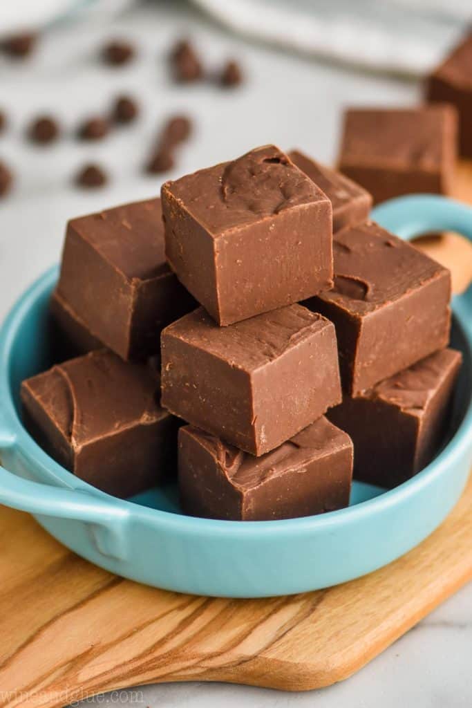 a pile of fudge in a small teal colored dish on a cutting board with chocolate chips in the background