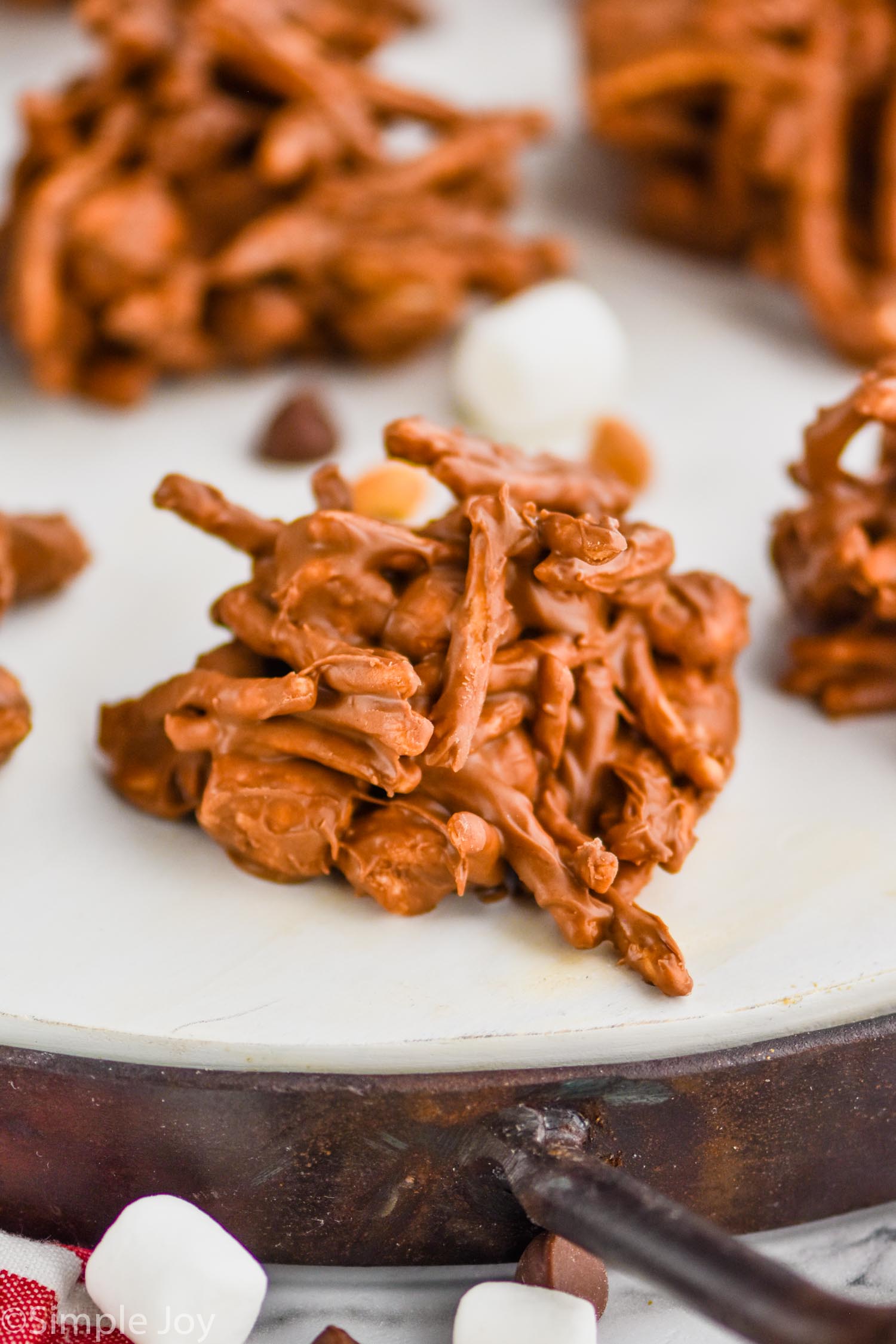 close up of a haystack cookie with peanuts, marshmallows, and chocolate chips blurred in the background