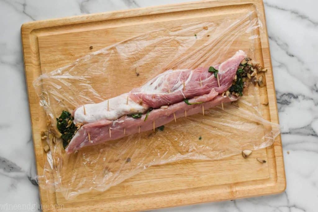 a pork loin that has been stuffed, rolled up, and is being held together with tooth picks before being roasted