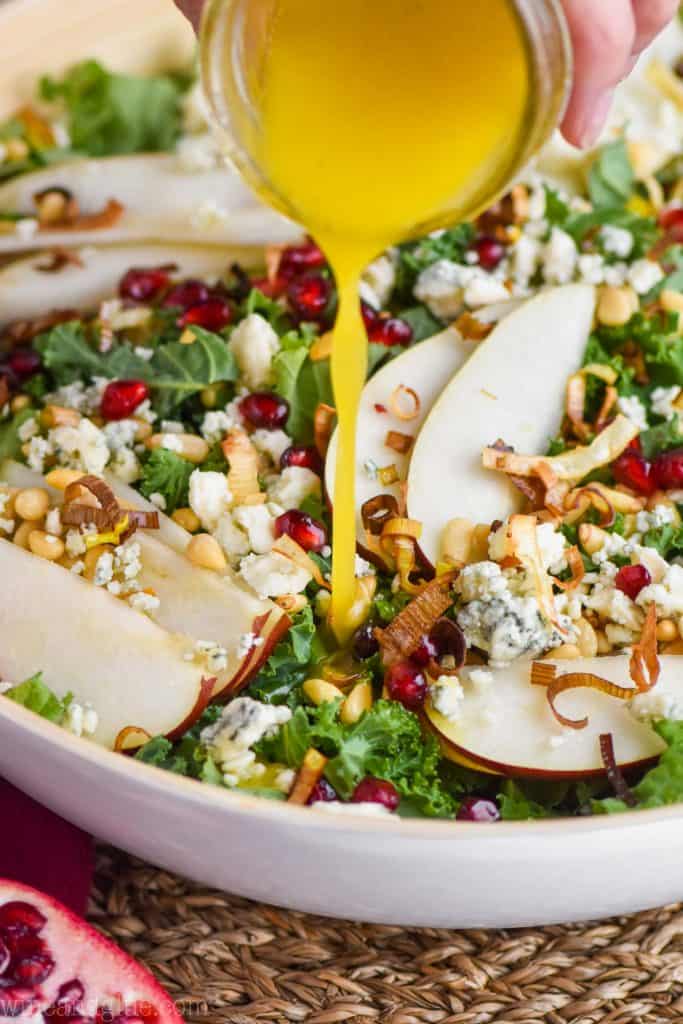 close up of a citrus dressing being poured on a winter salad in a white serving bowl