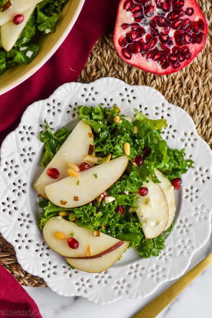 overhead view of a fancy white plate holding a kale salad recipe with sliced pears and pomegranate seeds