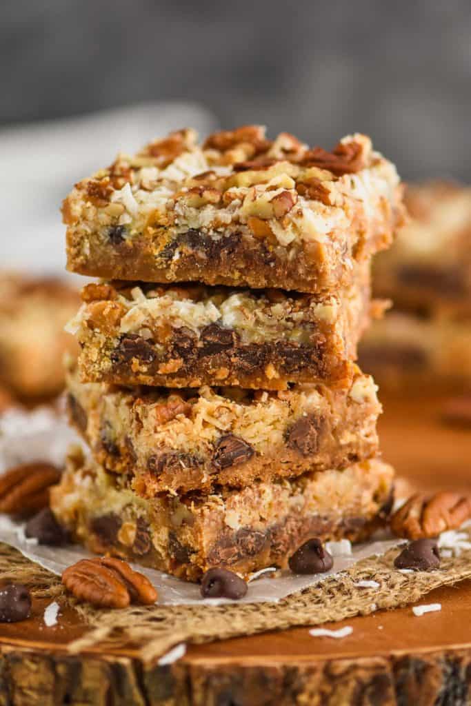 a stack of four magic cookie bars, layer of graham cracker, chocolate chip, coconut, and pecan pieces visible