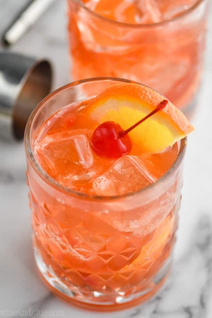 up close view of an old fashioned drink recipe with a ice cubes, a maraschino cherry, and an orange wedge