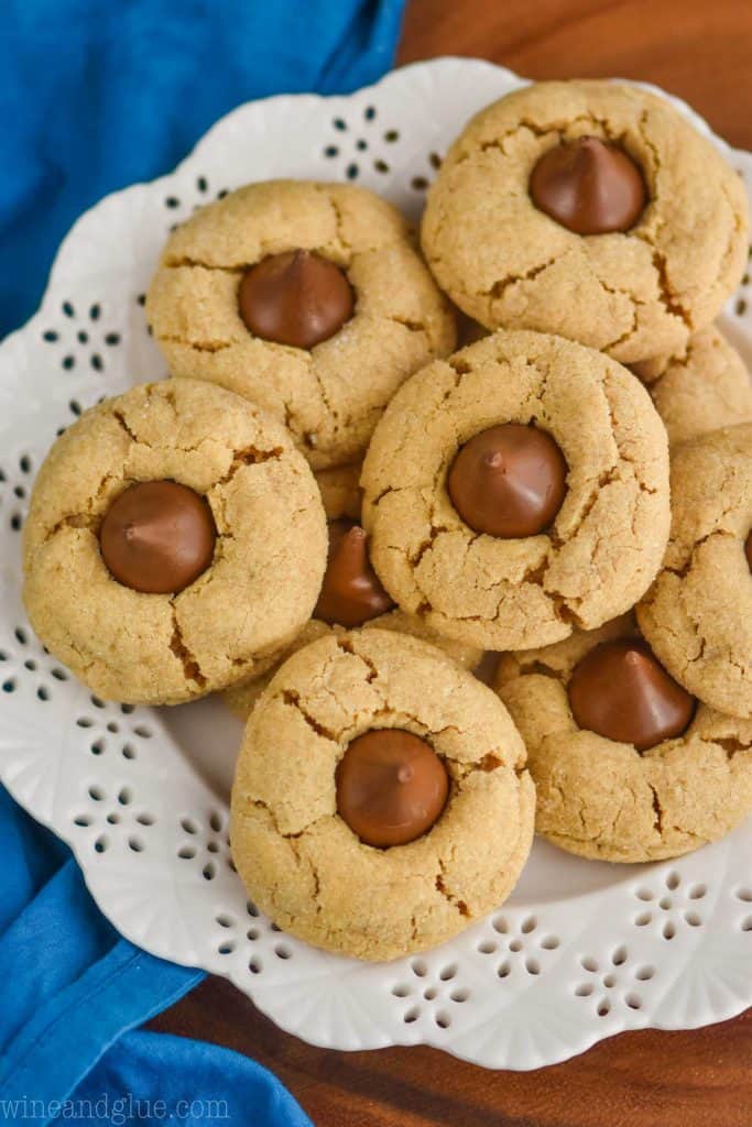 overhead view of peanut butter Hersey kiss cookies on a white detailed plate with a blue napkin and on a wood board