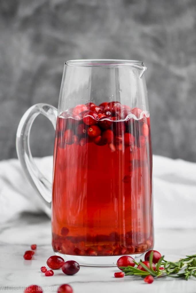 a tall pitcher filled with red holiday sangria with floating cranberries in it against a gray background