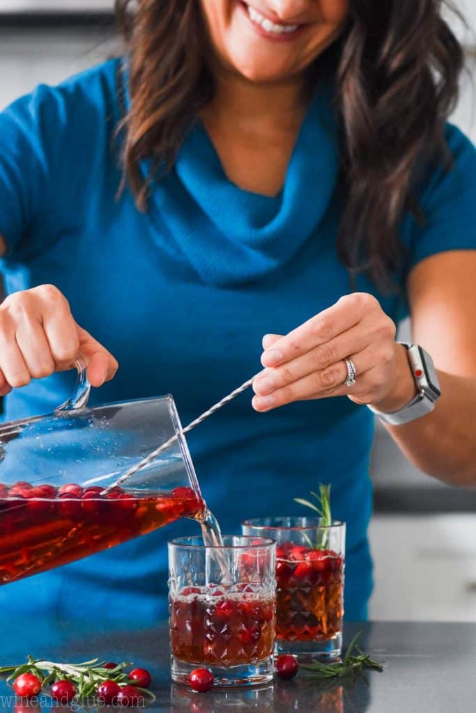 a woman wearing a blue sweater pouring a glass of red sangria
